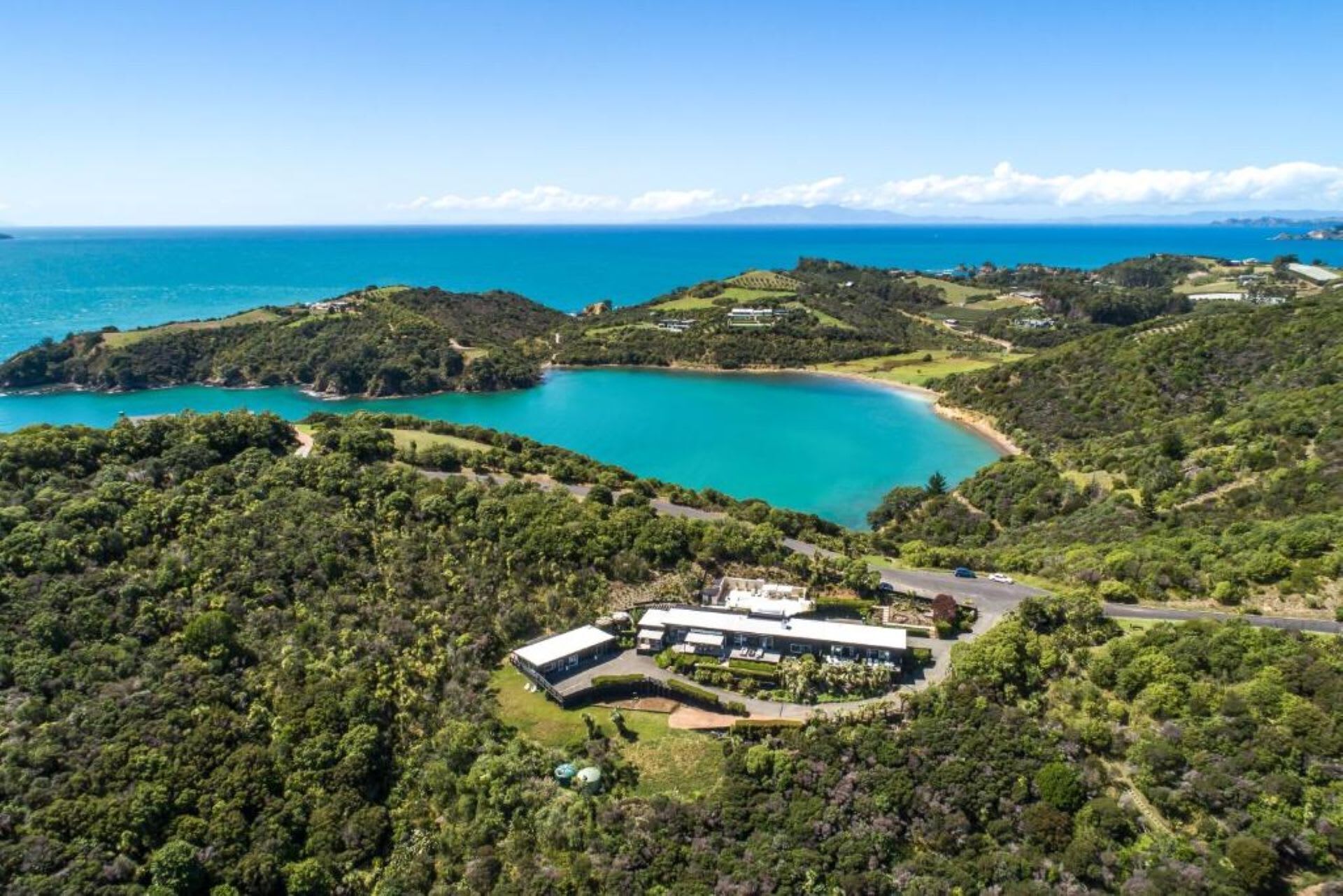 An aerial view of a coastal property with a large body of turquoise water, surrounded by lush greenery and hills.