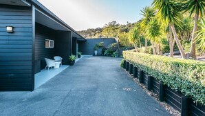 A modern building with a covered patio area, potted plants, and a well-maintained hedge. - Delamore Cove Kāraka Studio (Waiheke Island)