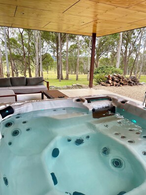 Un jacuzzi con cubierta de madera y un sofá bajo una pérgola, rodeado de árboles.