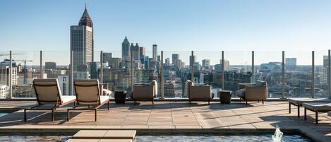 A rooftop terrace with lounge chairs and a pool, overlooking a city skyline.