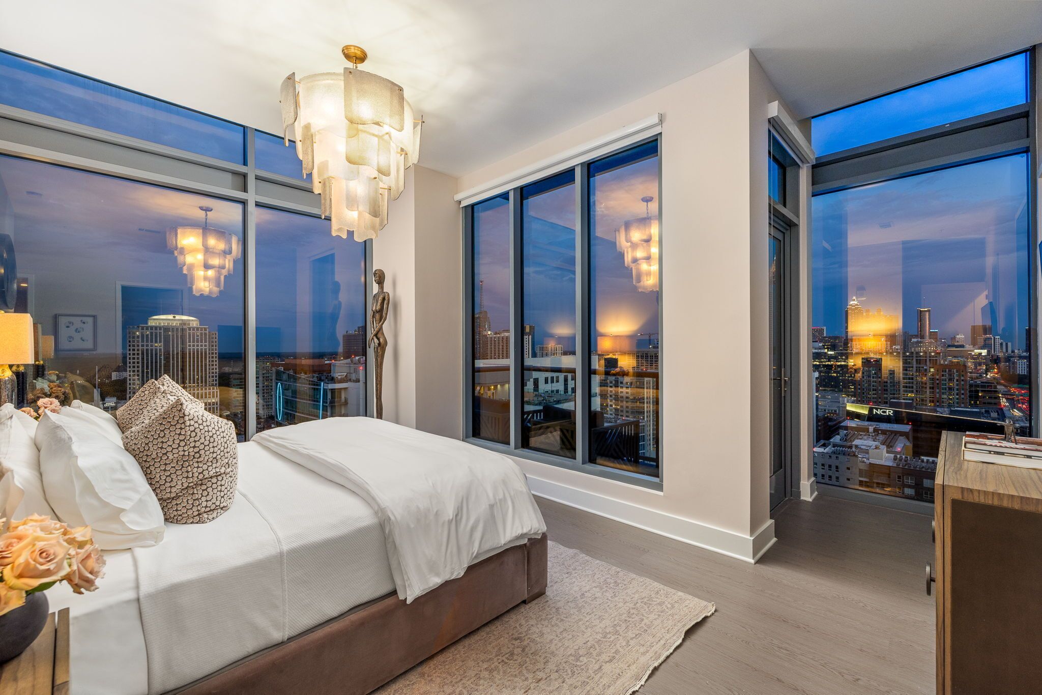 A modern bedroom with a large bed, a city view, and a chandelier.
