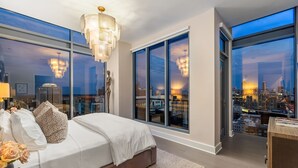 A modern bedroom with a large bed, a city view, and a chandelier. - 28th Floor Corner - Panoramic Penthouse by Atlanta Luxury Rentals (Atlanta)
