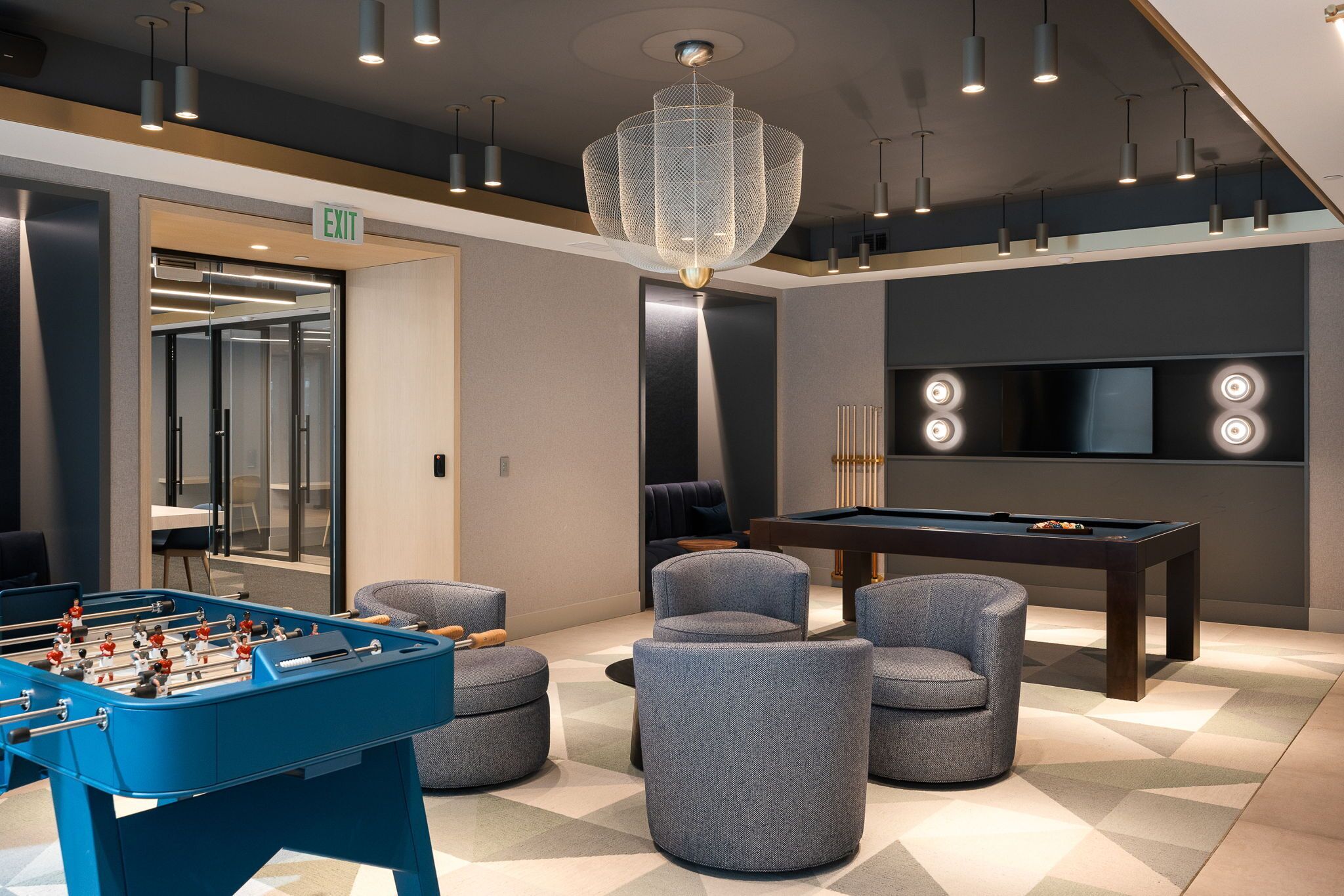 A modern lounge area with a foosball table, comfortable seating, a pool table, and a large TV screen.