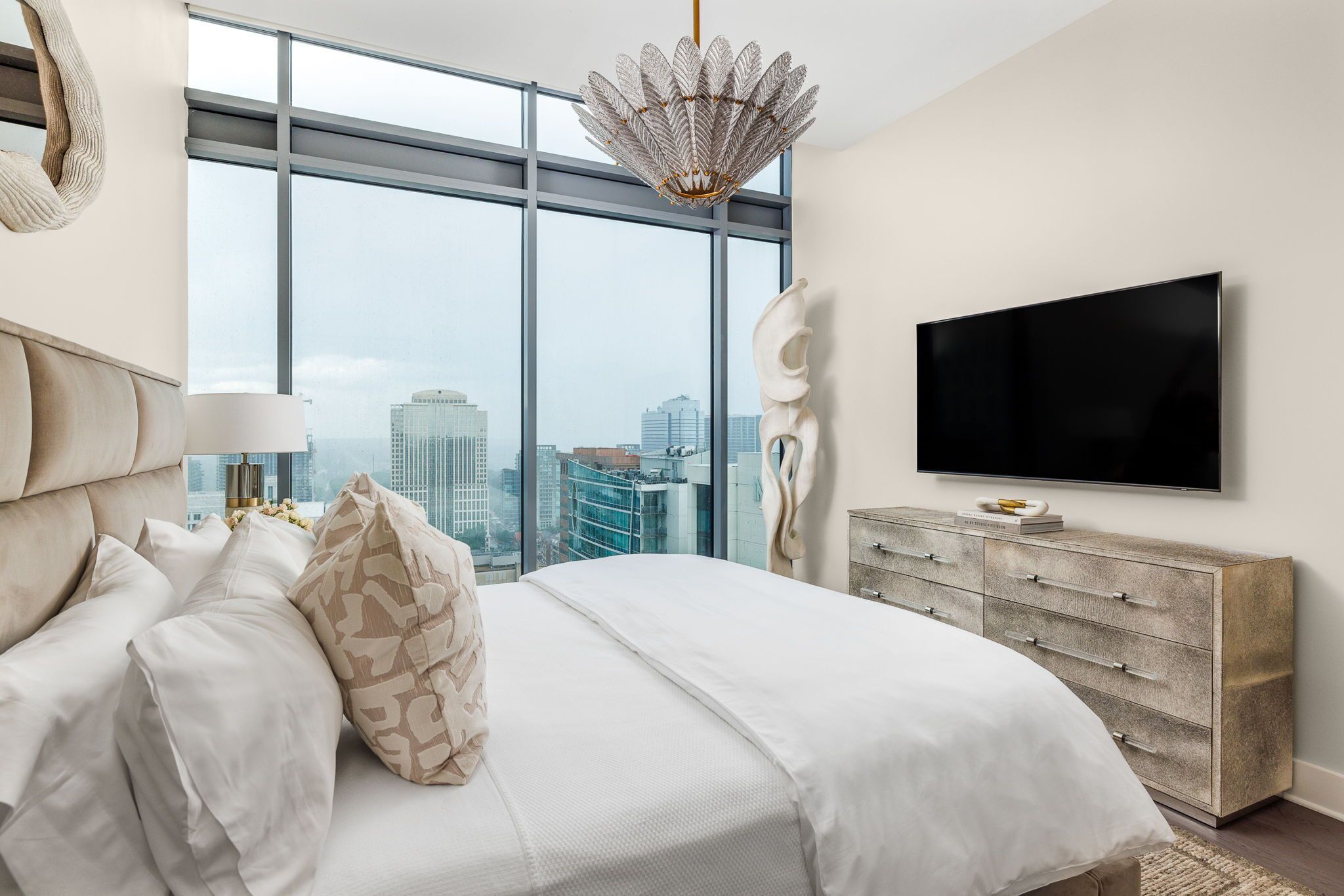 A modern bedroom with a large bed, a flat-screen TV, and a city view.