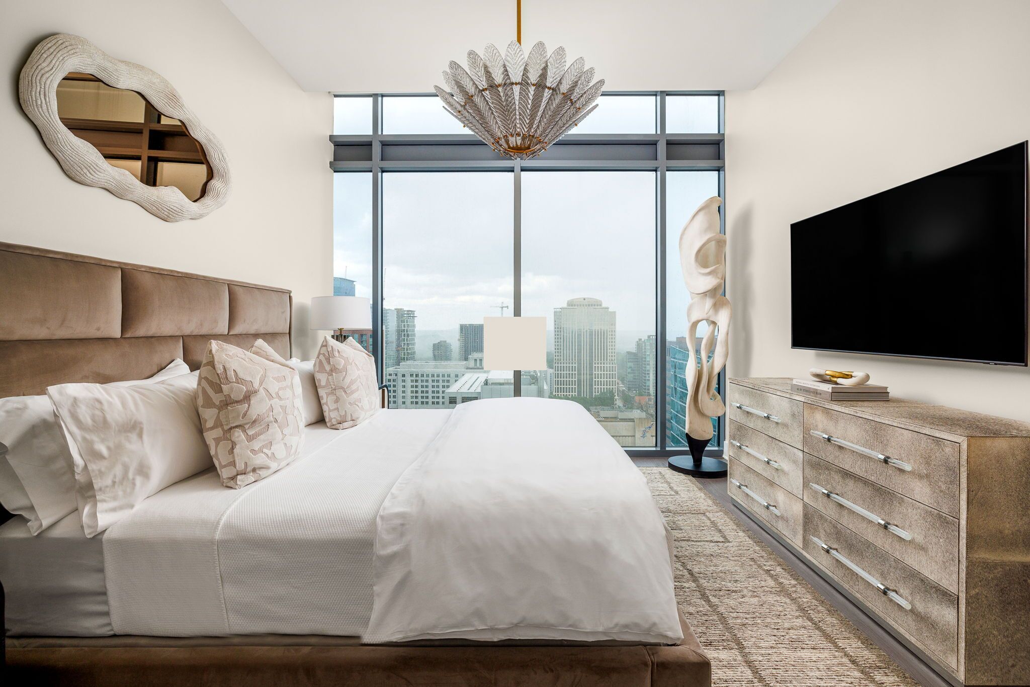 A modern bedroom with a large bed, a television, and a city view through large windows.