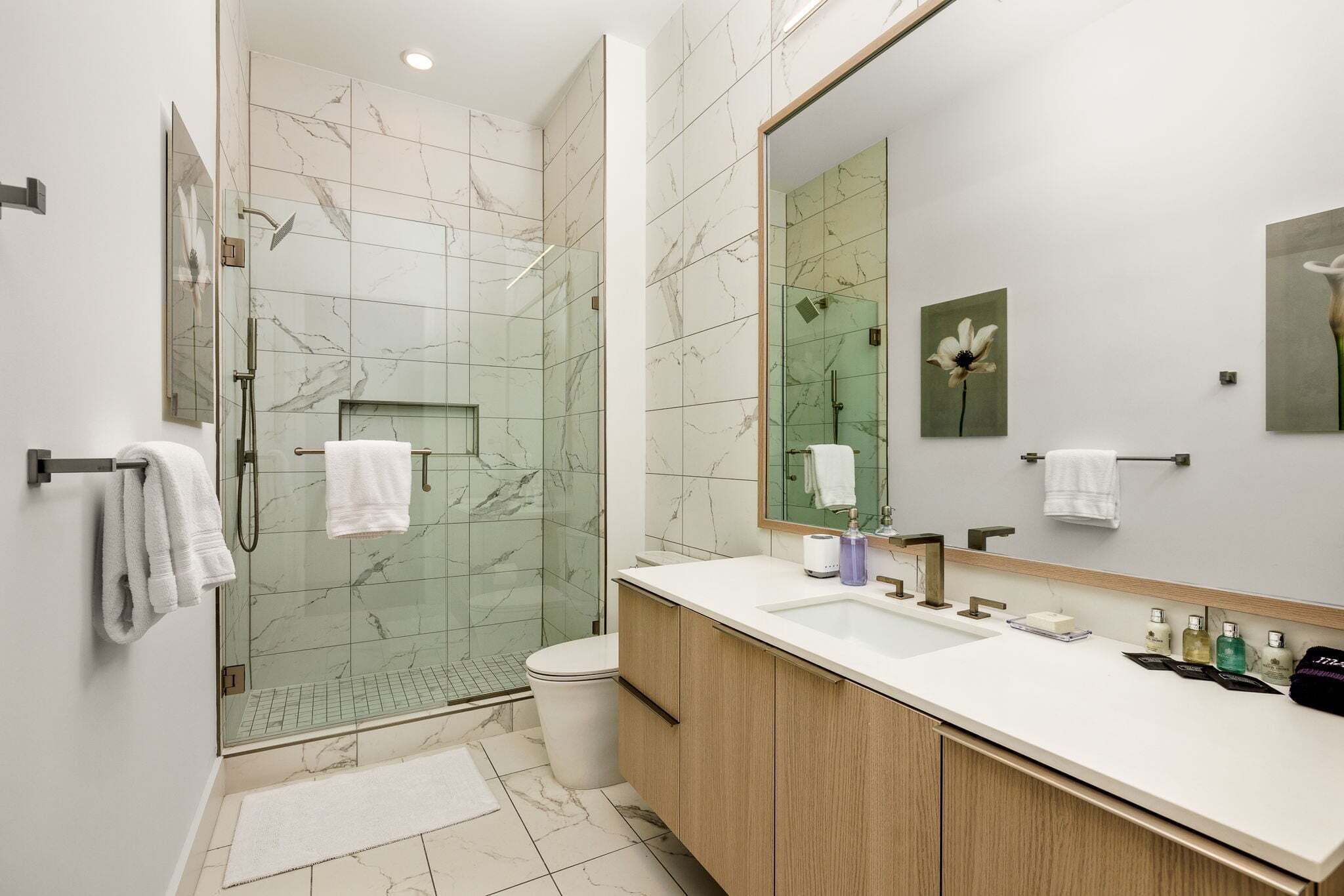 A modern bathroom with a glass-enclosed shower, a large mirror, and a wooden vanity with a white sink.