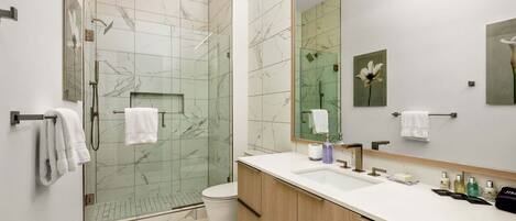A modern bathroom with a glass-enclosed shower, a large mirror, and a wooden vanity with a white sink.