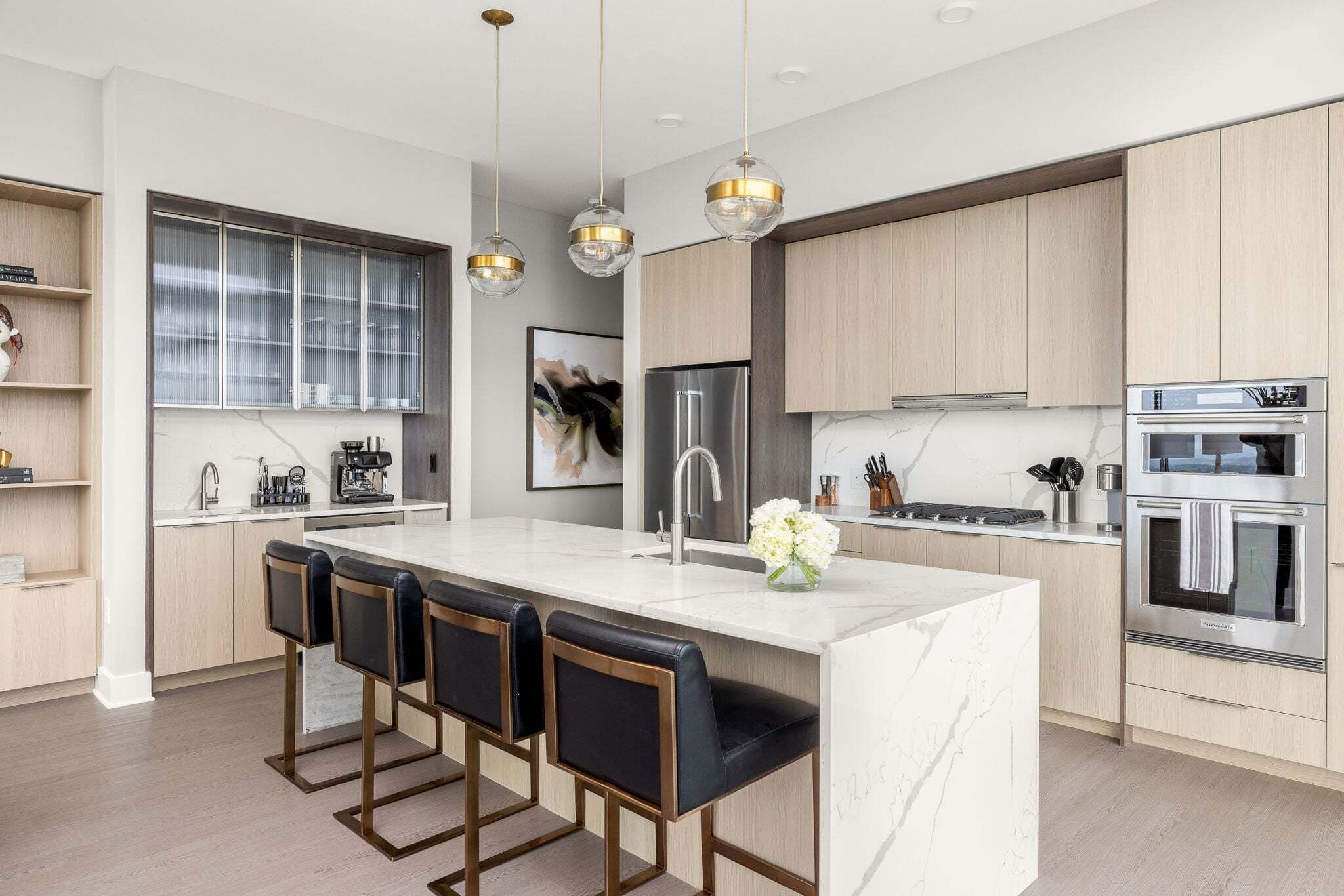 A modern kitchen with a central island, bar stools, stainless steel appliances, and pendant lighting.