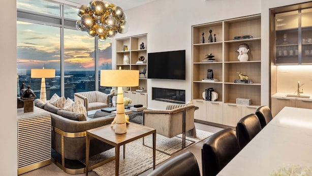 A modern living room with a sofa, armchairs, a coffee table, and a TV. There are shelves with decorative items and a fireplace. - 28th Floor Corner - Panoramic Penthouse by Atlanta Luxury Rentals (Atlanta)