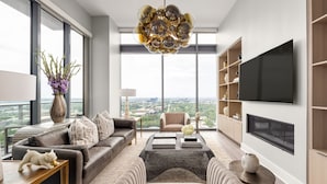 A modern living room with a large window, a chandelier, a flat-screen TV, and a sofa. - 28th Floor Corner - Panoramic Penthouse by Atlanta Luxury Rentals (Atlanta)