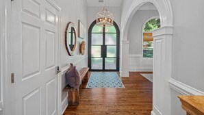 A hallway with white walls, wooden flooring, a bench, a patterned rug, and a large arched doorway with frosted glass panels. - Lake Effect by SoCharm | Pool & Spa, Waterfront (Mooresville)