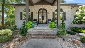 A brick house with a covered porch, a large arched doorway, and potted plants. - Lake Effect by SoCharm | Pool & Spa, Waterfront (Mooresville)
