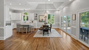 A spacious kitchen with a central island, wooden flooring, and large windows offering views of the outdoors. - Lake Effect by SoCharm | Pool & Spa, Waterfront (Mooresville)