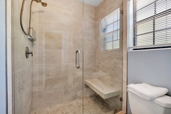 A modern bathroom with a glass-enclosed shower, a toilet with a towel, and a window with blinds.