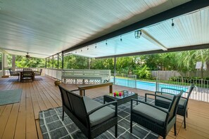 A covered outdoor area with a pool, wicker furniture, and a wooden deck.