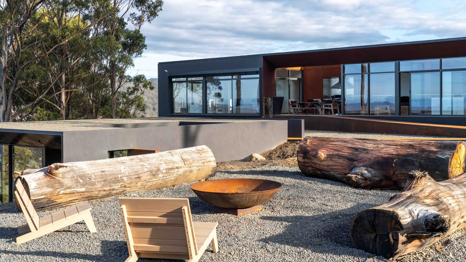 A modern building with large windows, outdoor seating, and natural wood logs.
