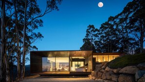A modern, glass-enclosed building with a visible interior, surrounded by trees and a rocky landscape, under a night sky with a visible moon. - Mountain Top Snug Whole Property Itas (Snug)