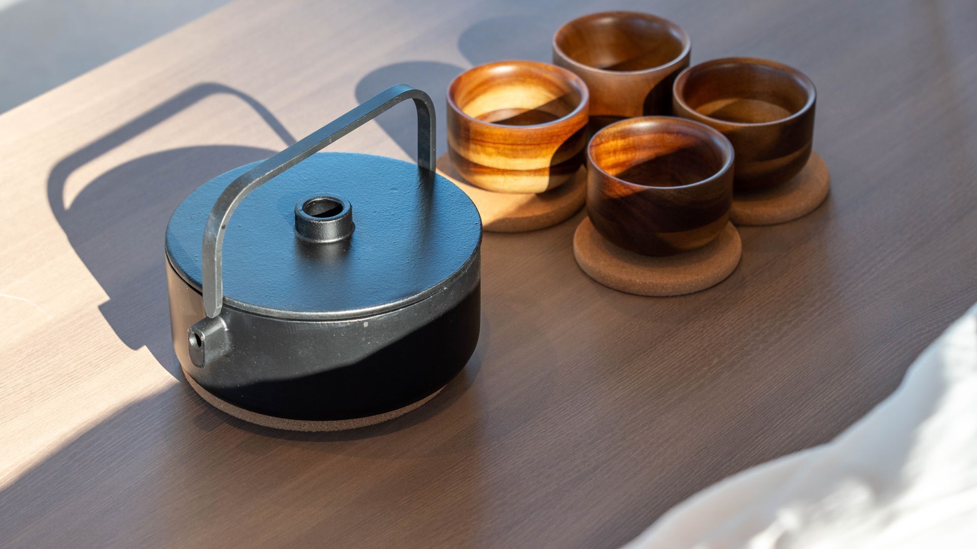 A black teapot with a handle and spout, accompanied by four wooden cups on coasters.