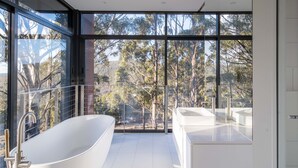 A modern bathroom with a freestanding bathtub, a large window, and a view of trees. - Mountain Top Snug, House Itas (Snug)