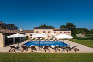 A swimming pool with lounge chairs and umbrellas, surrounded by a well-maintained lawn and a large building in the background.
