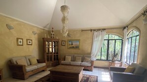 Un salón espacioso con techo alto, piso de baldosas y ventanas grandes con cortinas.