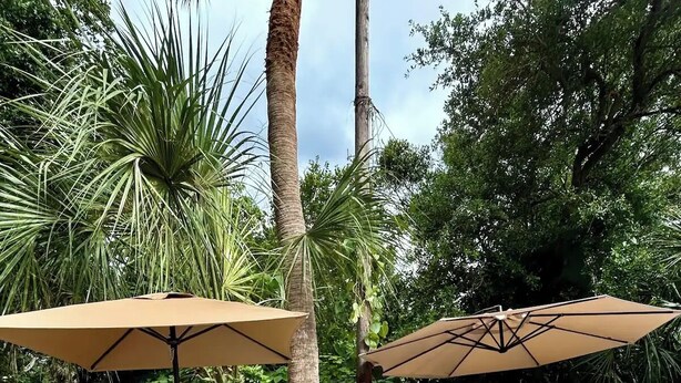 Une terrasse extérieure avec une table à manger et des chaises, deux grands parasols et un ensemble de meubles de jardin en osier.
