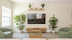 Un salon doté d’un grand téléviseur à écran plat, d’un meuble de rangement en bois et de plusieurs plantes en pot.