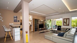 A modern living room with a sofa, a dining area, and a kitchen visible through an open door.
