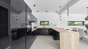 A modern kitchen with a central island, black cabinets, and a large window. - Villa MaEm (Istria - Škicini) (Škicini)
