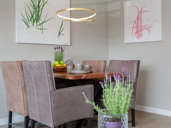 Un espace repas comprenant une table en bois, des chaises rembourrées et un luminaire suspendu.