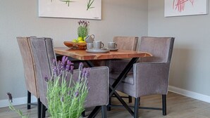 A dining area with a wooden table, grey upholstered chairs, and a glass vase with purple flowers. - Strand Brise - "Strand-Brise" vacation apartment in Westerland, in a prime location (Sylt)