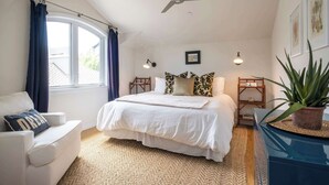 Ein Schlafzimmer mit einem großen Bett, einem Deckenventilator, einem Fenster mit Vorhängen, einem Nachttisch mit Lampe und einer Topfpflanze.
