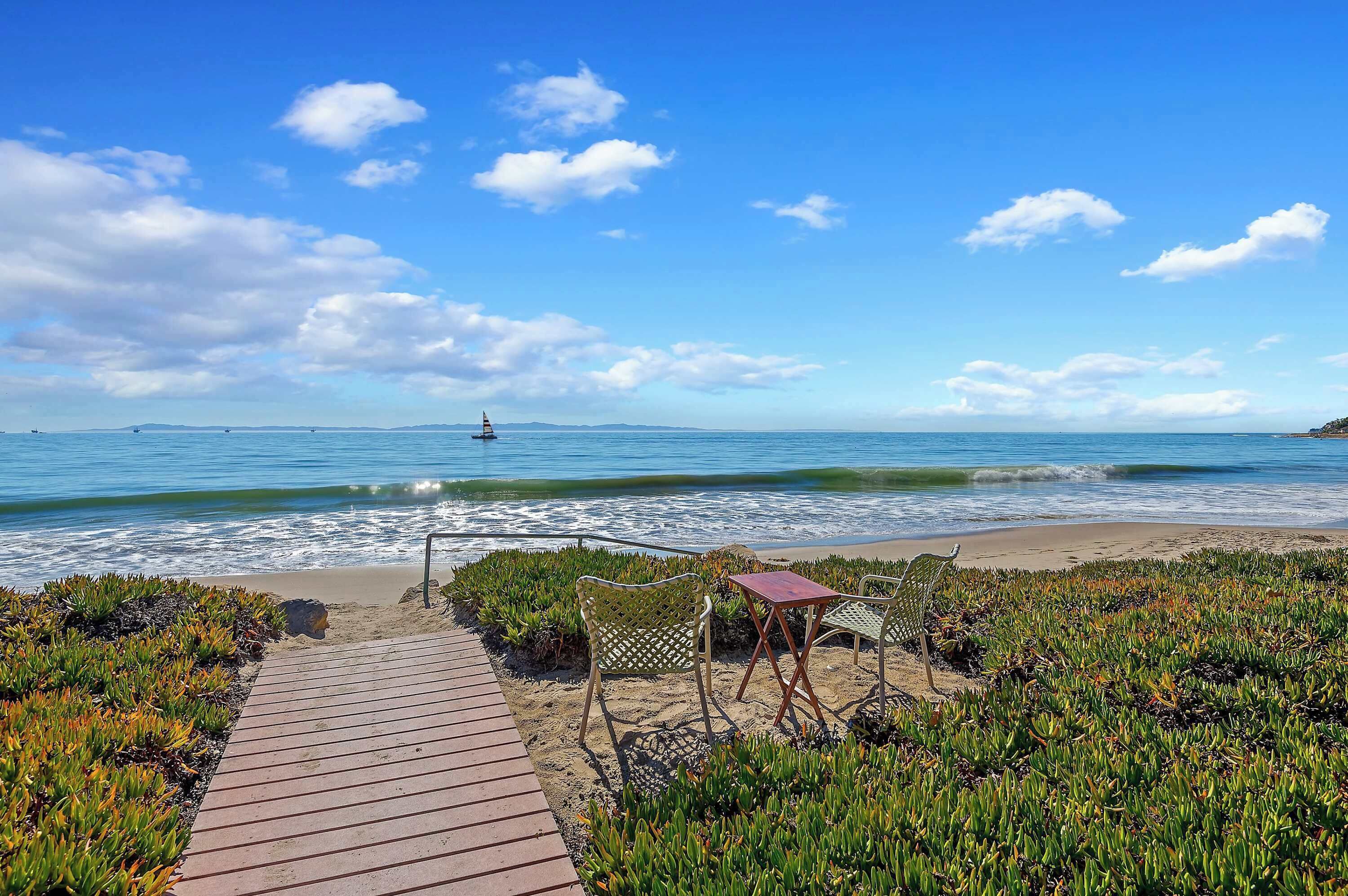 Une plage avec une promenade en bois menant à un espace aménagé avec des chaises et une table.