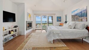 A bedroom with a bed, a TV, a bookshelf, and a balcony with a view.