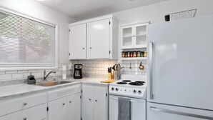 A modern kitchen with white cabinets, a stove, a sink, and a coffee maker. - Snug Spot 68: Cozy 1-Bedroom Retreat near Downtown Eugene & Autzen! (Eugene)