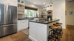 Une cuisine moderne avec des meubles blancs, des appareils en acier inoxydable et un îlot central doté de tabourets de bar.