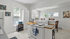 Una cocina con muebles blancos, estufa, microondas y un comedor con mesa y sillas de madera.