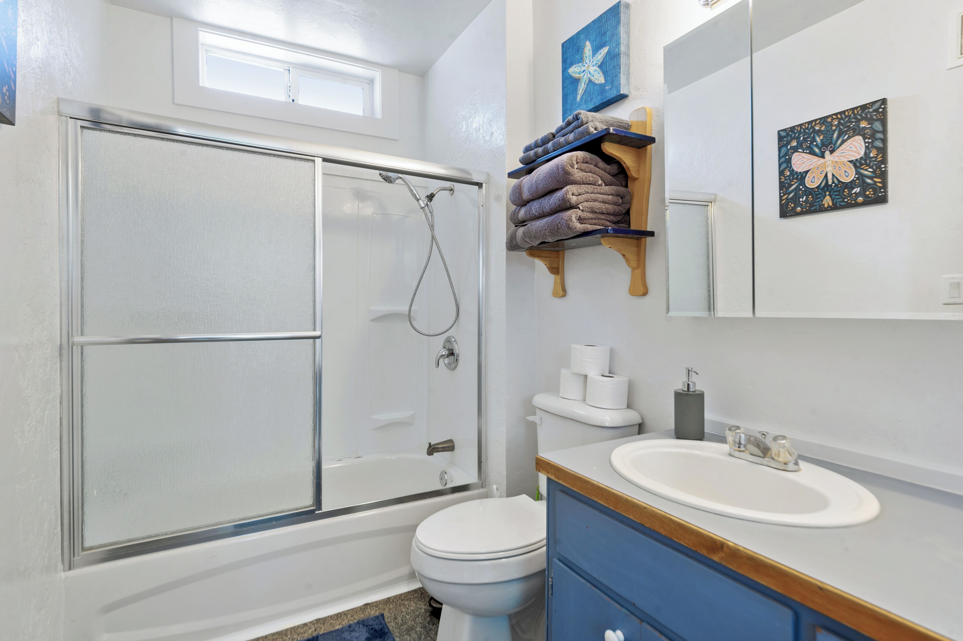 A bathroom with a glass shower enclosure, a toilet, a sink, and a towel rack with towels.