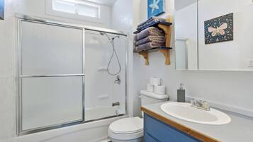 A bathroom with a glass shower enclosure, a toilet, a sink, and a towel rack with towels.
