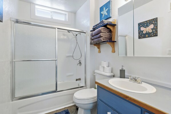 A bathroom with a glass shower enclosure, a toilet, a sink, and a towel rack with towels.