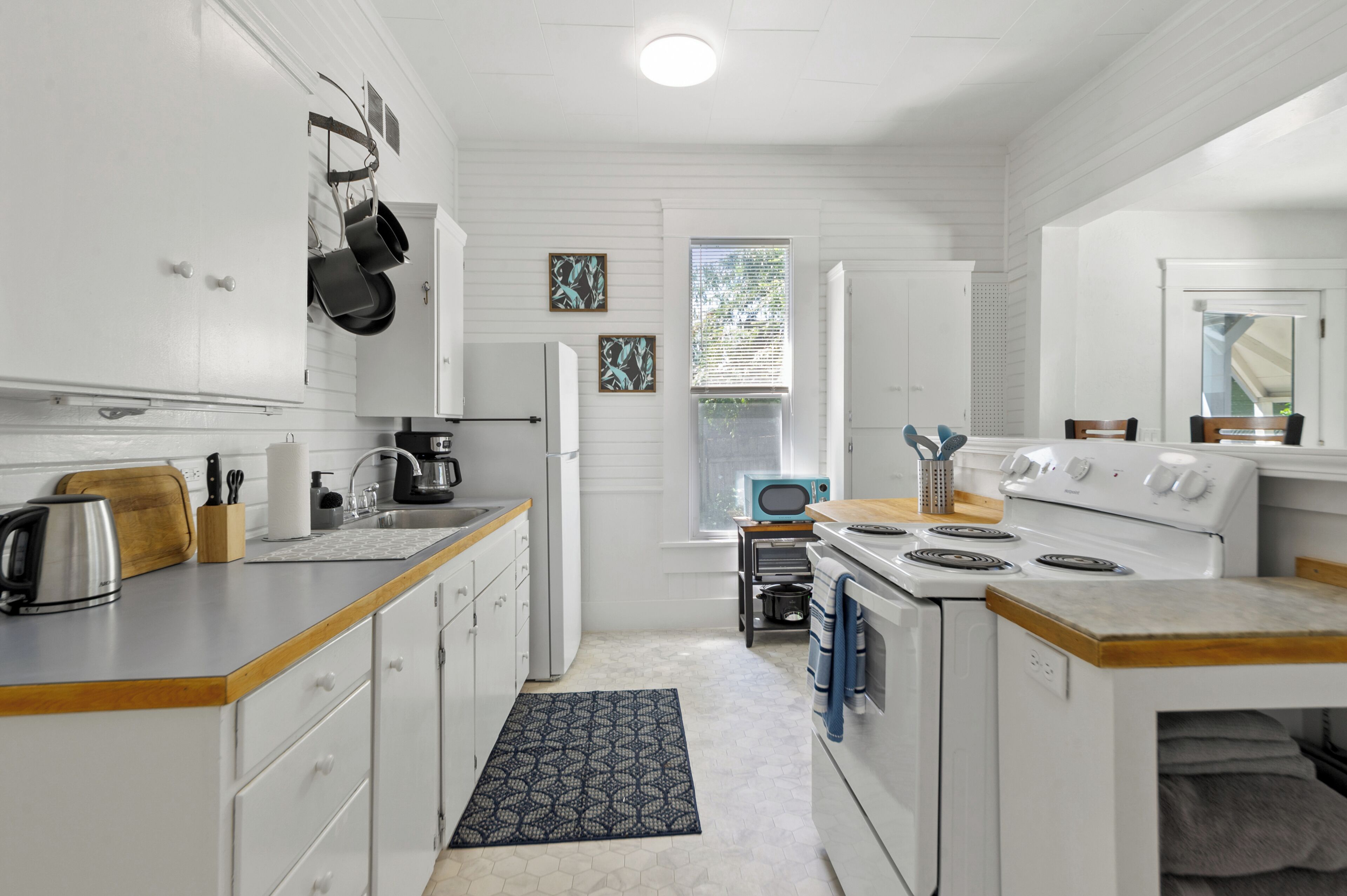 Una cocina moderna con armarios blancos, estufa, lavamanos y ventana con persianas.