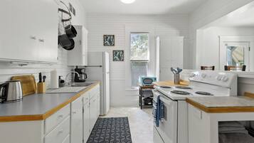 Una cocina moderna con armarios blancos, estufa, lavamanos y ventana con persianas.
