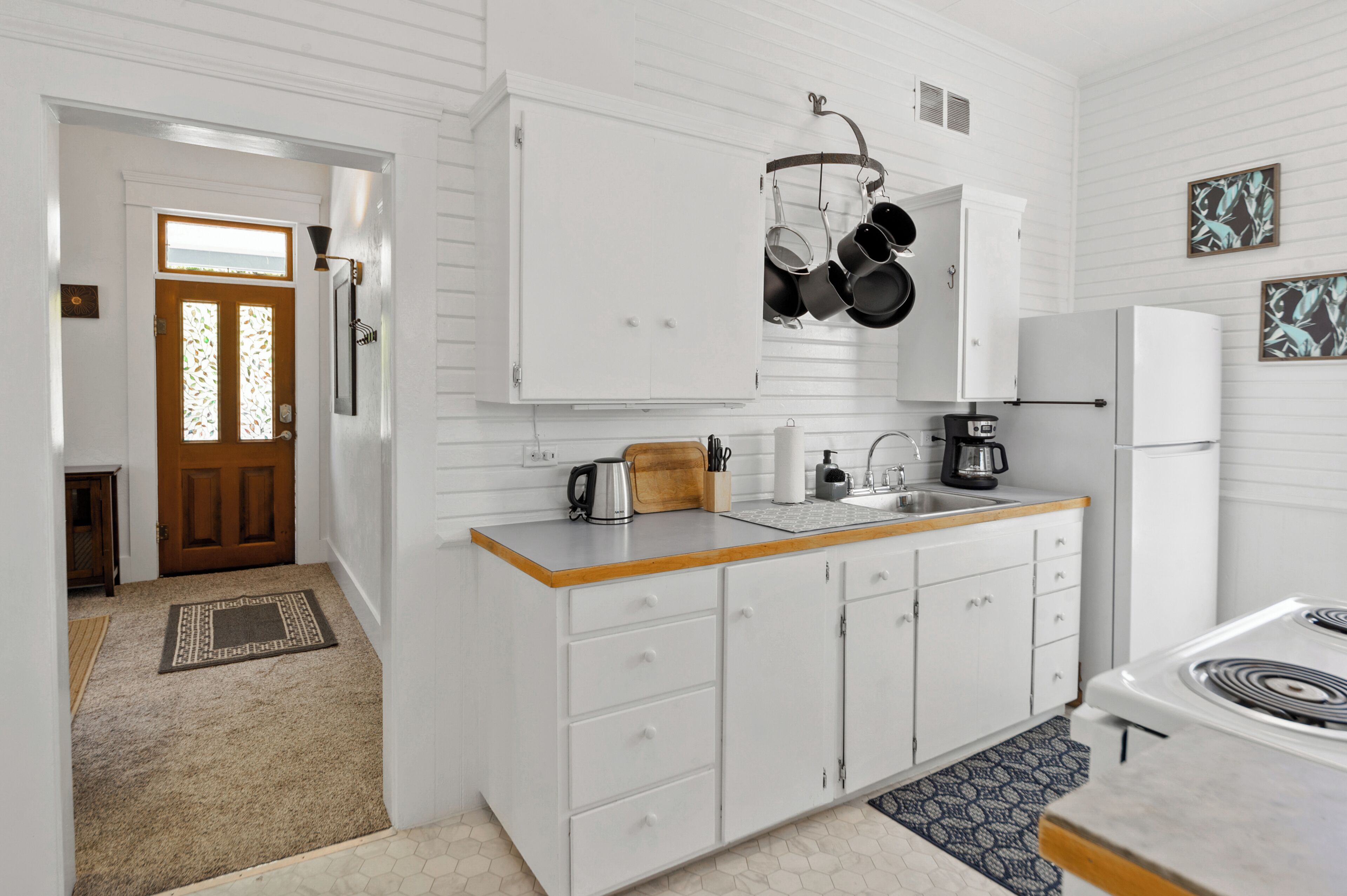 A kitchen with white cabinets, a wooden countertop, a stove, and hanging pots.