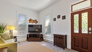 Una sala de estar con televisor, sofá, mesa de centro, alfombra, aparador y puerta con vidrieras.