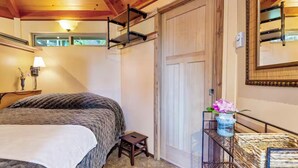 A bedroom with a bed, a small stool, a nightstand, a lamp, a window, and a door.