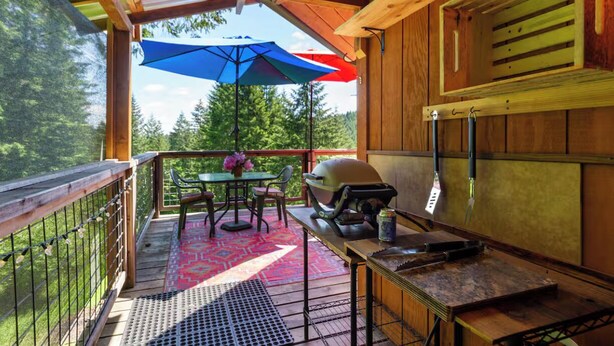 A wooden deck with a grill, table, chairs, and a blue umbrella.