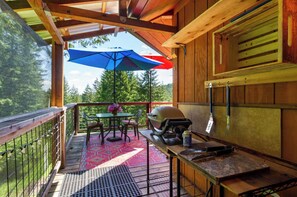 A wooden deck with a grill, table, chairs, and a blue umbrella. - Hillside Deck Cottages: A cozy, rustic PNW retreat perfect for 4. (Junction City)