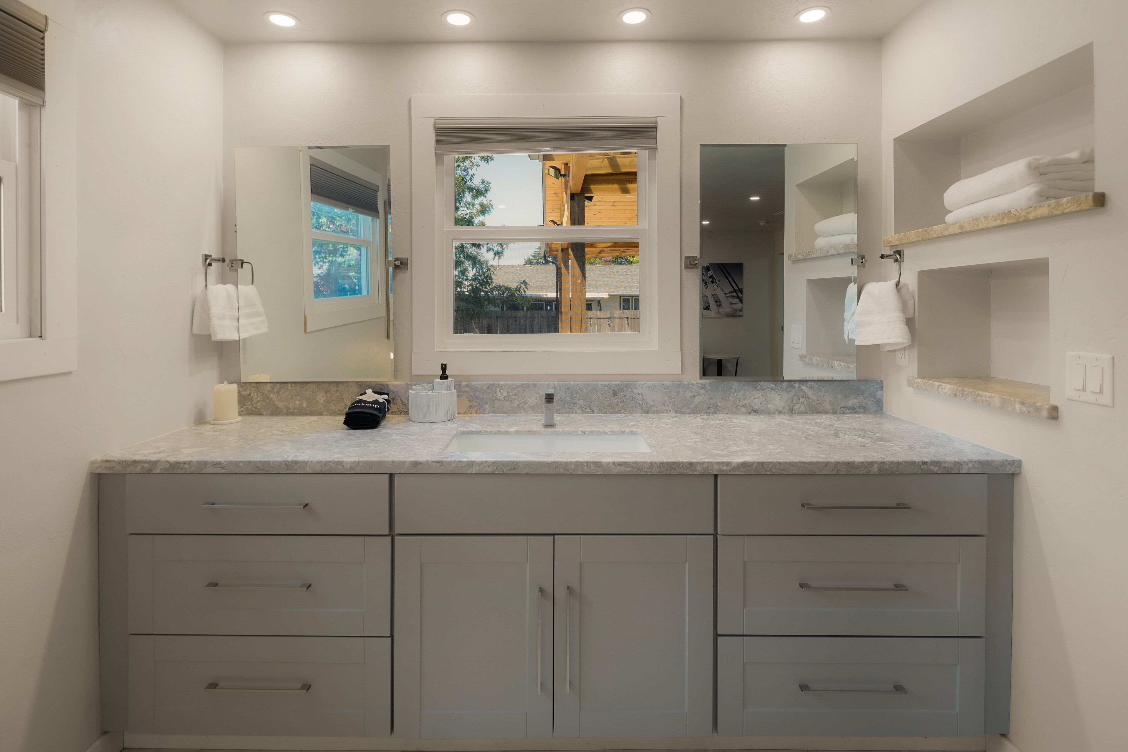 A modern bathroom with a large sink, multiple drawers, a mirror, and a window with a view.