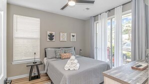 Una camera da letto con un letto, una ventola a soffitto, una finestra con tende e vista sull'esterno.