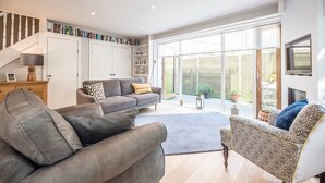 A modern living room with a grey sofa, patterned armchair, and a bookshelf filled with books. - Skimming Stones, Southwold (Suffolk)